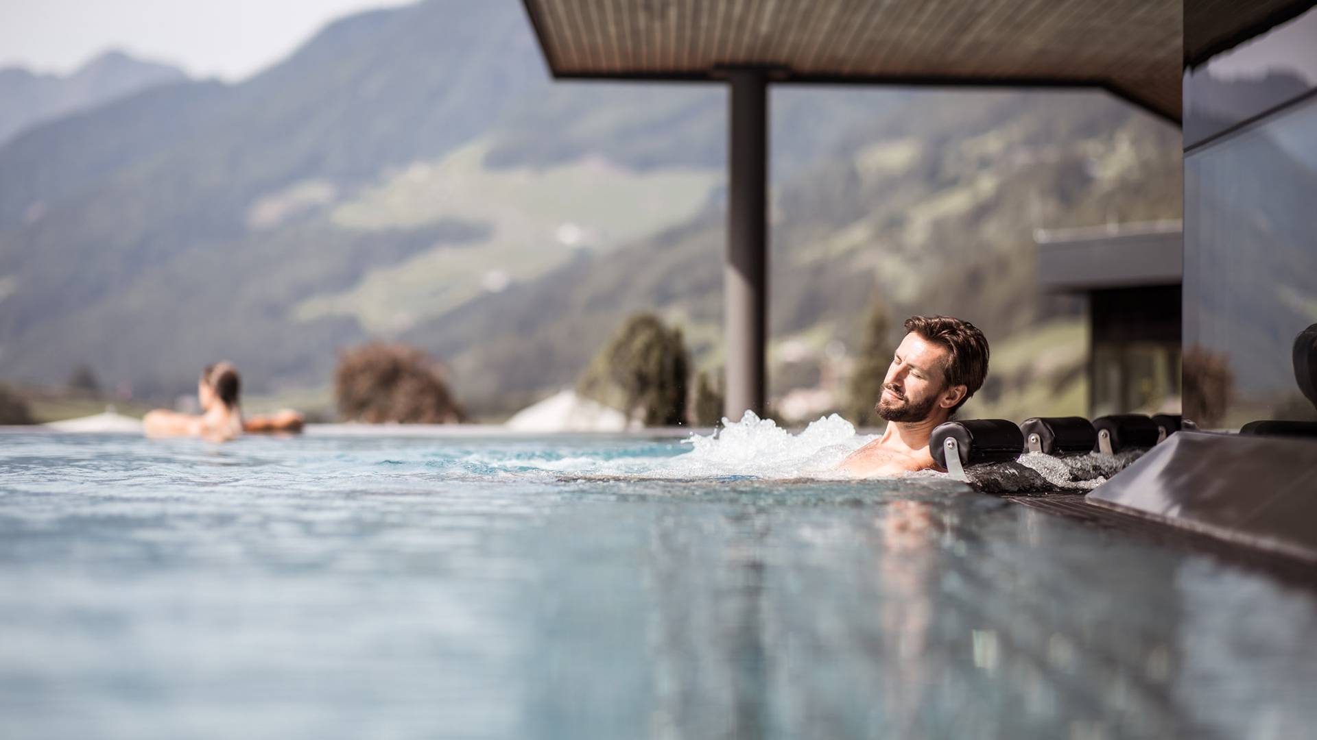 Mann liegt im Infinity Whirlpool mit Alpenpanorama im Spa & Wellness Bereich des A&L im Ahrntal