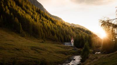 Kirche im Ahrntal an einem Fluss und Wald im Sonnenuntergang