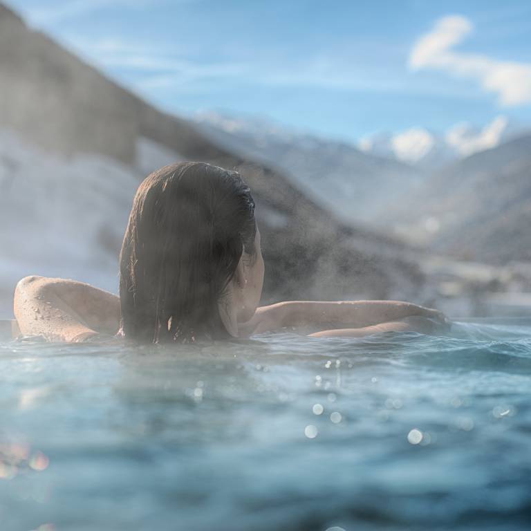 Frau entspannt im Aussenpool des A&L Wellnessresort und schaut auf das Ahrntal