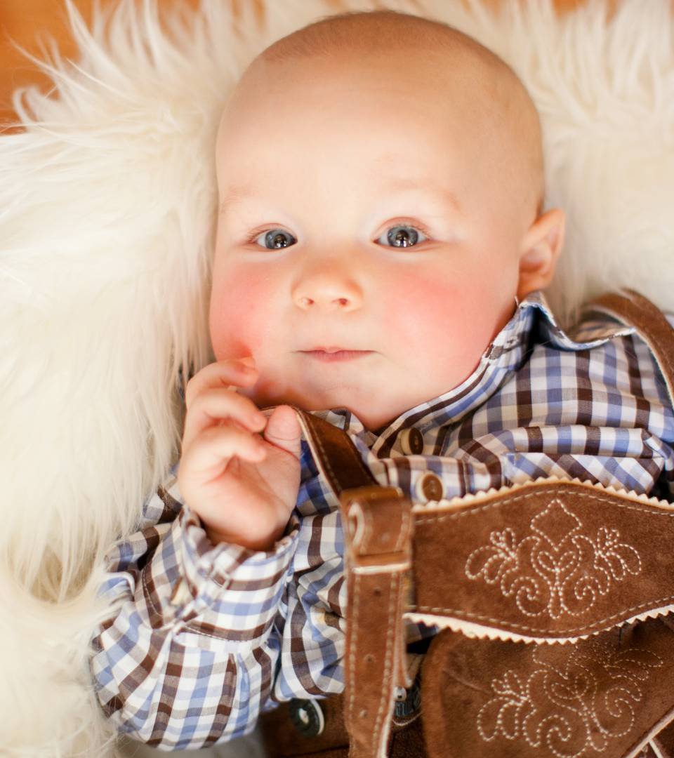 Baby in traditionellen Lederhosen liegt auf einem Fell